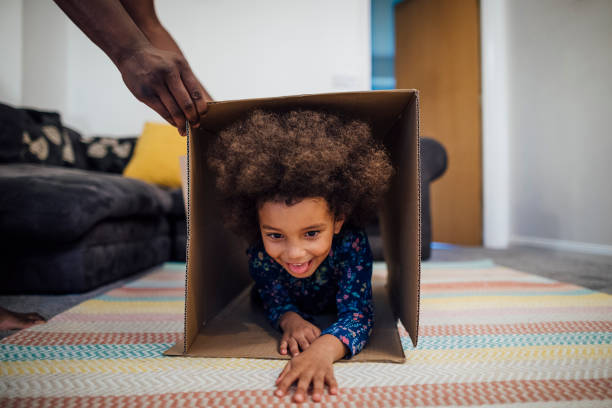 Ready, Set, Go! Mixed race girl crawling through a cardboard box in the sitting room at home, her unrecognisable father is holding the box up for her. obstacle course stock pictures, royalty-free photos & images