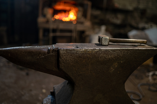 A blacksmith's hammer lies on an anvil against the background of a burning forge.