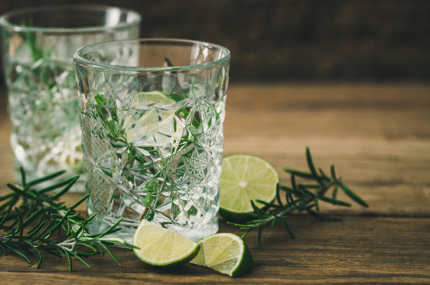 bicchieri con una rinfrescante bevanda al rosmarino al lime, metà lime e rami di rosmarino su legno vecchio - hot drink alcohol green glass foto e immagini stock
