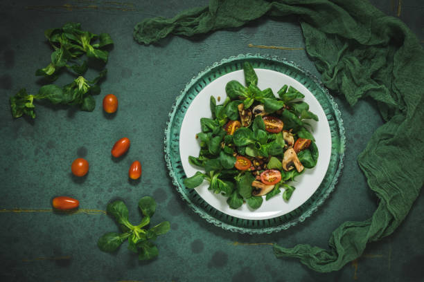 Fresh corn salad with mushrooms and roasted seeds on a white plate on green background, top view