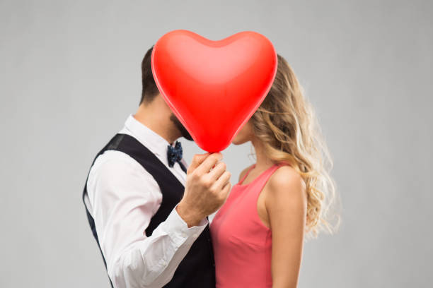 istock couple hiding behind red heart shaped balloon 1284888400