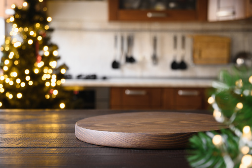 Wooden tabletop with cutting board and blurred modern kitchen with Christmas tree.