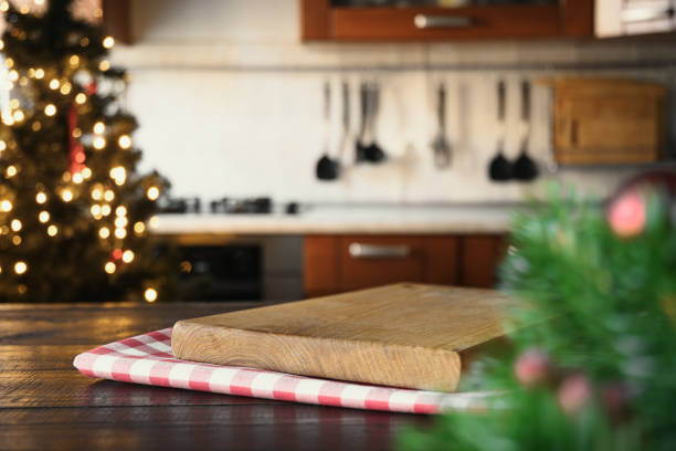 istock Wooden tabletop with cutting board and blurred modern kitchen with Christmas tree. 1284888557