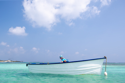 A small child plays on a boat in the lagoon of a tropical island