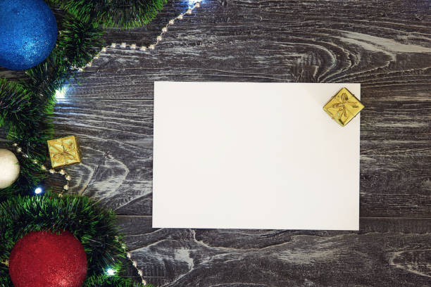 istock Horizontal paper blank with christmas frame at left. Flat lay. New year card gift. Balls, presents, snowballs, green and red tinsel. On grey wooden background. Top view 1284890706