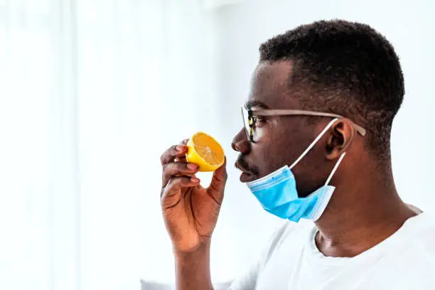 One African man Trying to Sense Smell of a Lemon at home during the day, smell blindness is one of the possible symptoms of covid-19.