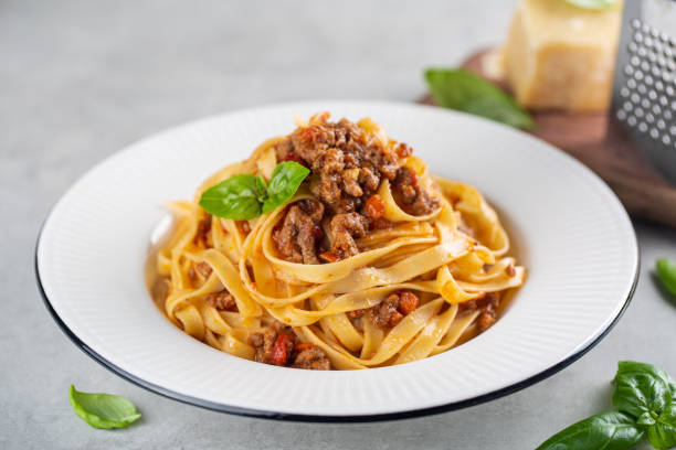 tagliatelle al ragu - итальянская паста с мясным соусом болоньезе. высокий ангел. дополнительный твердый сыр на заднем плане. - pappardelle стоковые фото и изображения