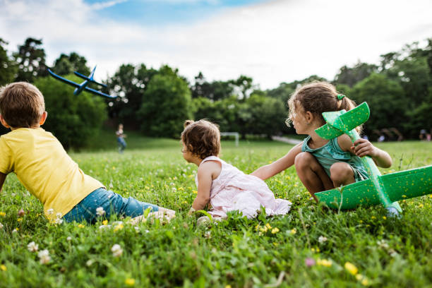 Boy and two girls are catching a plane in the meadow field. Leisure games.