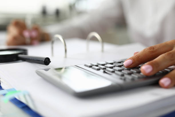 istock Women's hands on calculator next to magnifying glass and documents 1284897572
