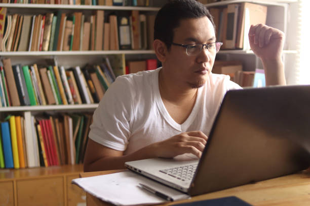 istock Asian man studying in library, exam preparation concept. Male college student using laptop to learn online 1284898560
