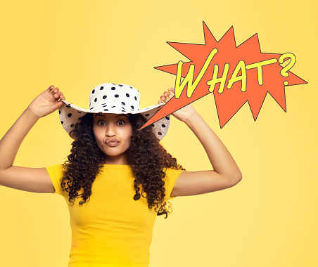Beautiful quirky mixed race teenager in her white dotted hat isolated on yellow background with a speech bubble saying \
