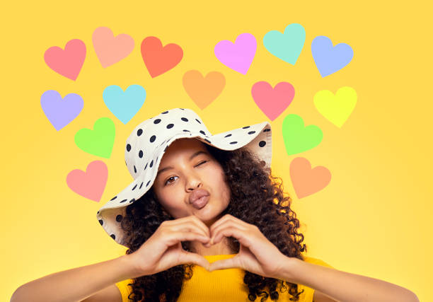 Beautiful mixed race teenager showing heart with hands Kissing portrait of beautiful mixed race teenager showing heart with hands in her white dotted hat isolated on yellow background cute 15 year old girls stock pictures, royalty-free photos & images