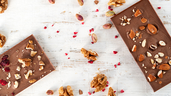 Homemade delicious milk chocolate bars with sublimated raspberries almond and walnut on white wooden background. Flat lay. Horizontal orientation.