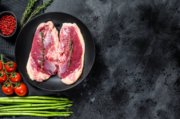 istock Raw duck Breasts on a plate. Organic poultry meat. Black background. Top view. Copy space 1284901947