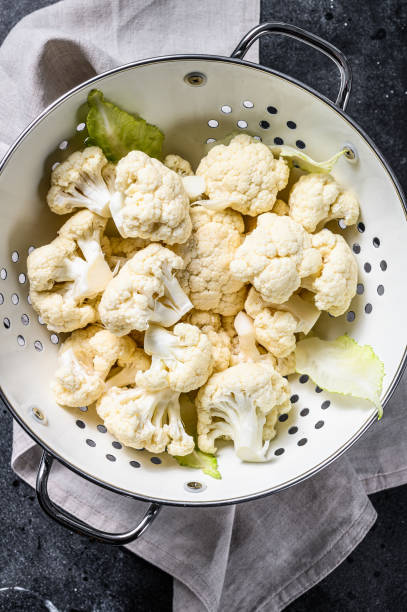 istock Fresh white heads cleaned cauliflower in a colander. Black background. Top view 1284903037