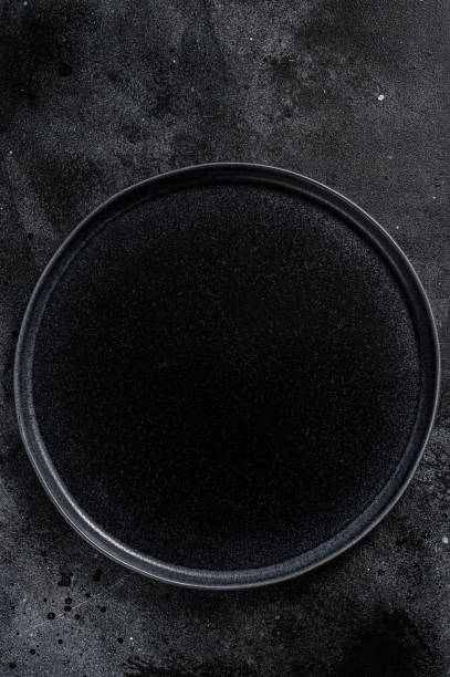 istock Round Black plate  on textured black background.  Top view. Copy space 1284904975