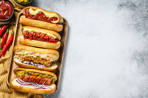 Hot dogs fully loaded with assorted toppings on a tray. Delicious hot-dogs with pork and beef sausages. White background. Top view. Copy space.