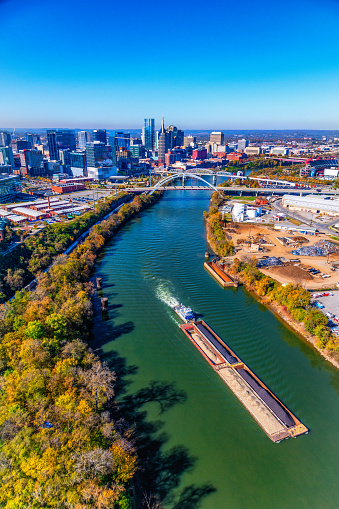 A tug boat and barge on the Cumberland River near the downtown skyline of beautiful Nashville, Tennessee, also known as \