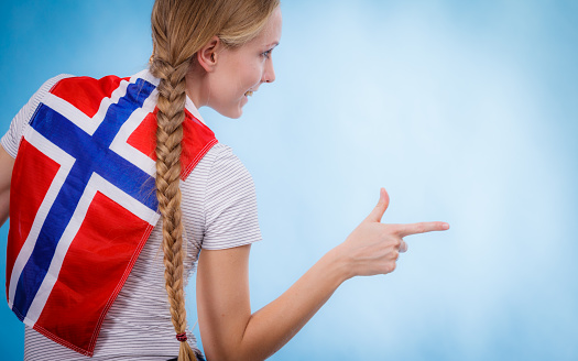 Blonde girl braid hair with norwegian flag on her back, female pointing with finger to copy space text area. Scandinavian people.