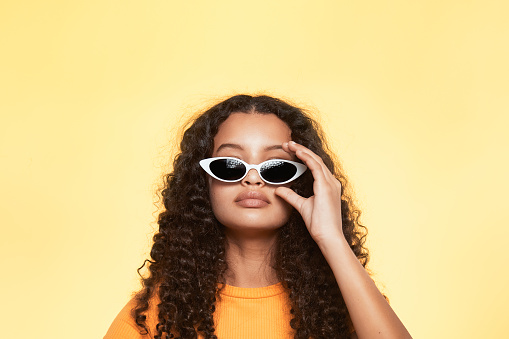 A portrait of a beautiful teenager with white sunglasses, isolated on yellow studio background