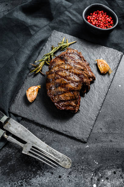 istock Grilled Flat Iron steak on a stone Board, marbled beef. Black background. Top view 1284908233