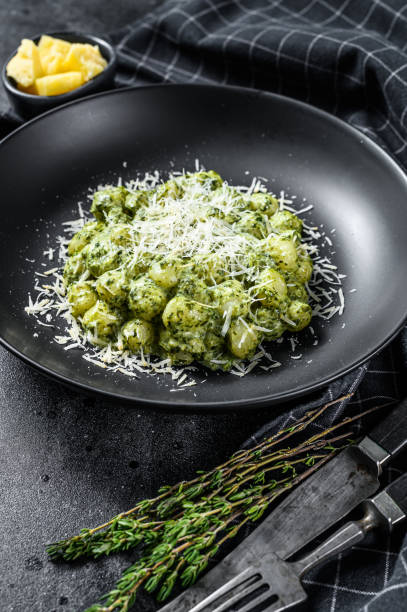 istock Gnocchi with basil spinach sauce and Parmesan. Italian potato paste. Black background. Top view 1284908328