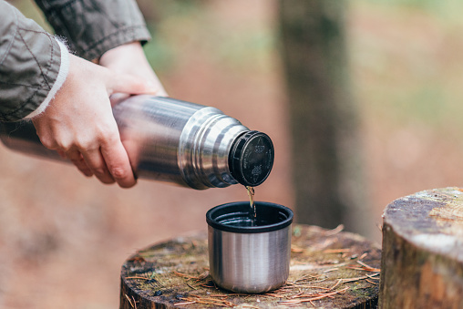 Female hands holding thermos and pouring hot tea into a mug