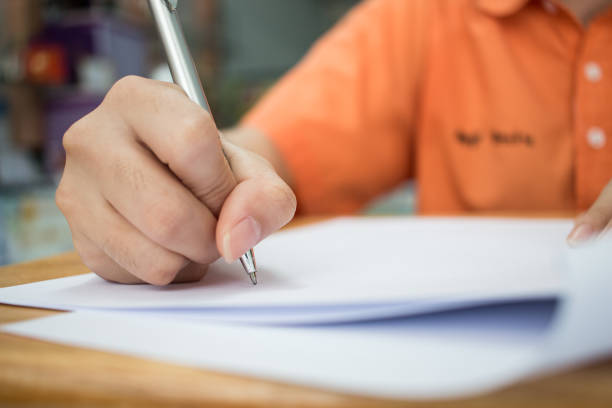 istock School Students hands taking exams, writing examination room with holding pencil on optical form of standardized test with answers and english paper sheet on desk doing final exam in classroom. 1284908611