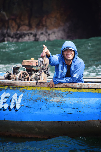 Paracas, Peru - October 22 2018: Local Peruvian fisherman in his blue boat shows up his catch this early morning - an octopus - with a proud smile. Photo taken near Ballestas Islands outside Paracas, Peru.