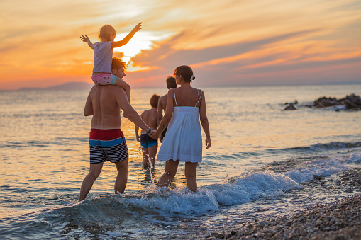 Rear view of family of five enjoying beach at scenic sunset