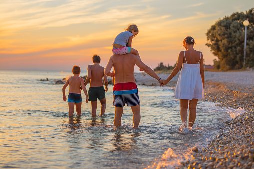 Rear view of family of five enjoying beach at scenic sunset