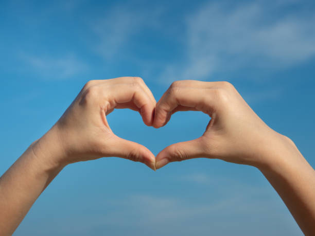 istock Heart symbol from hands on the blue sky background. 1284920986