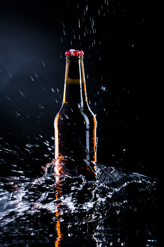 Water splashing over a beer bottle on dark background