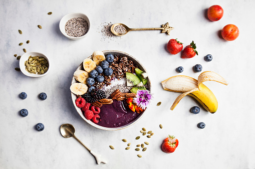 Top view of açai bowl with fresh fruits for breakfast with banana, blueberries, blackberries, strawberries, kiwi, nuts and seeds.