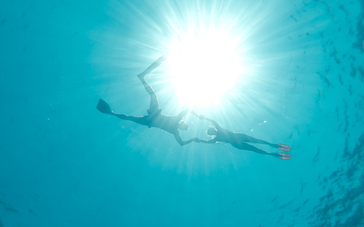 Low angle view of two people swimming in blue sea wearing swim fins