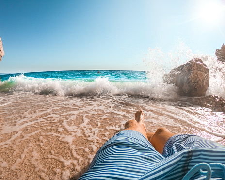 Legs of man lying on sandy beach stroked by sea waves