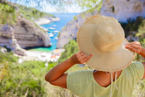 Rear view head and shoulders shot of a female tourist in a sun hat on vacations on the beach with cliffs