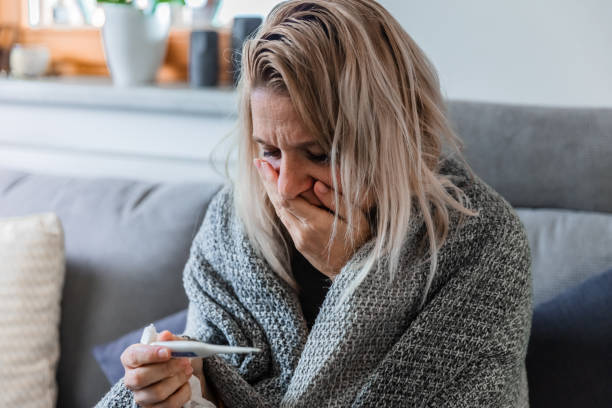 istock A sick woman looking at thermometer on the couch 1284926173