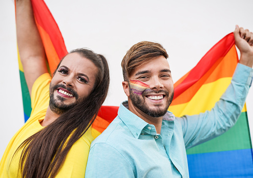 Young gay man and female impersonator with rainbow flag at gay pride parade
