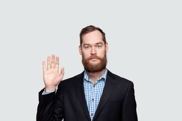istock Bearded man in suit raising hand over grey background 1284935756