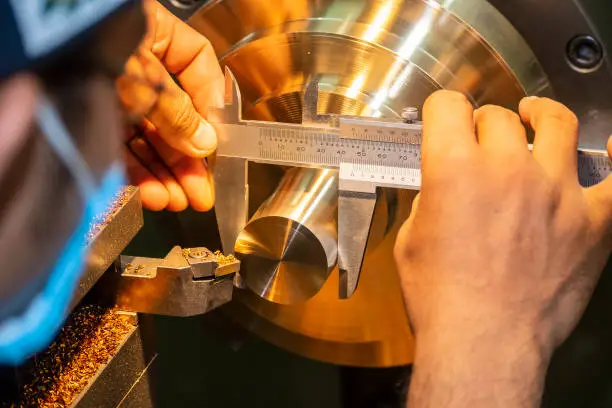 Photo of The machine operator measure the dimension of brass shaft by Vernier caliper.