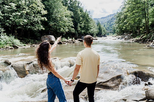 Love story of couple. Travelling in Karpathian mountains and feeling freedom. Waterfall in mountain river. Cascade waterfall and happy couple. Girl is pointing her boyfriend