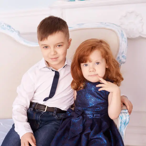 Brother and sister. Bright interior. Blue dress. Square.