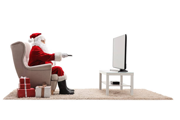 full length profile shot of santa claus in armchair with a remote control watching tv - remote television movie box imagens e fotografias de stock