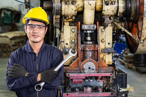 Portrait of a workman wearing yellow helmet in front of machine.