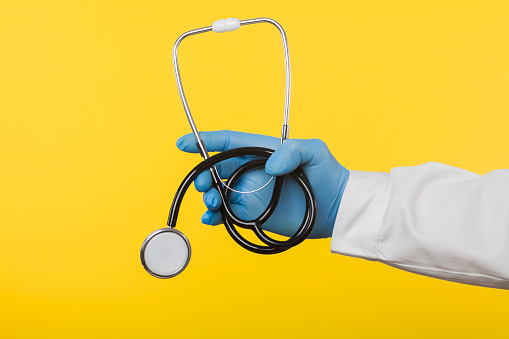Doctor in a protective glove holding a stethoscope isolated on a yellow background