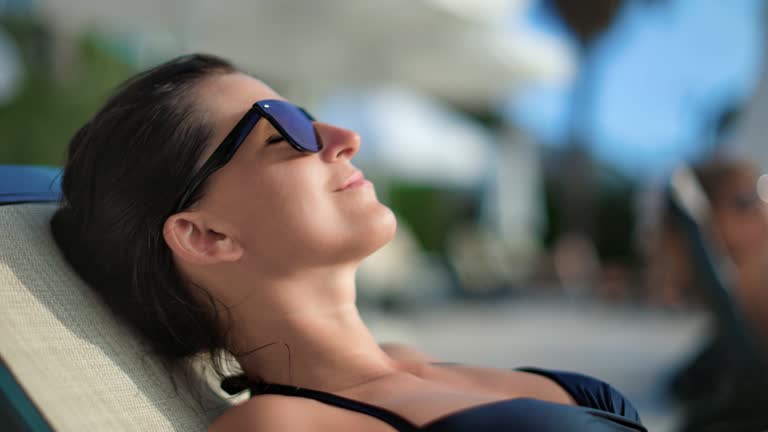 Closeup face of woman in sunglasses sunbathing on deck chair. Medium close up shot on 4k RED camera