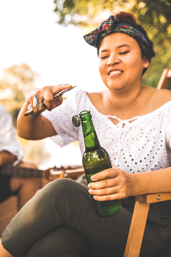 Three quarter length shot of happy young woman opening a bottle of beer to enjoy with her friends on a picnic in nature.