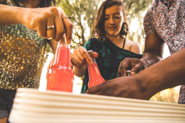 Low angle view of three young people taking out bottles of refreshing alcoholic beverages from a cooler while having a picnic in nature.