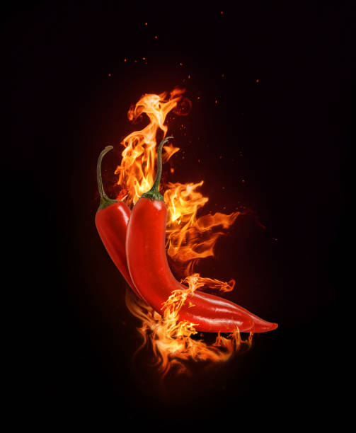 istock Two red chili peppers in a burning flame on a black background. 1284951851